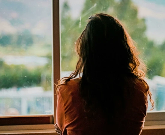 Woman looking out of a window at a blurred natural landscape